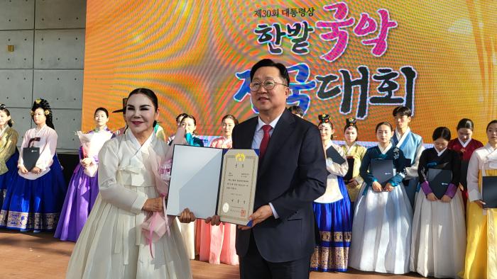 제30회 한밭국악전국대회에서 대통령상을 수상한 김정희 평화어울예술단 단장이 상장을 들고 기념촬영을 하고 있다 뒤편에는 단원들이 함께 무대에 올라 기쁨을 나누고 있다