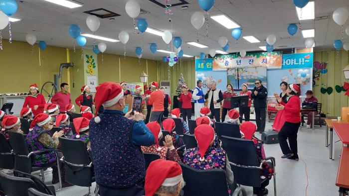 해피누리 봉사단의 공연으로 무대와 객석의 경계가 허물어지며 노아실버센터 송년잔치에 참석한 어르신들과 출연진이 함께 어우러져 손뼉을 치고 노래를 따라 부르는 흥겨운 시간이 이어지고 있다 2025년 12월 19일 노아실버센터 송년잔치